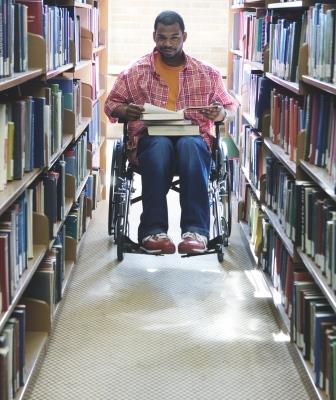 a person who is black, male, and a wheelchair user in a narrow library aisle